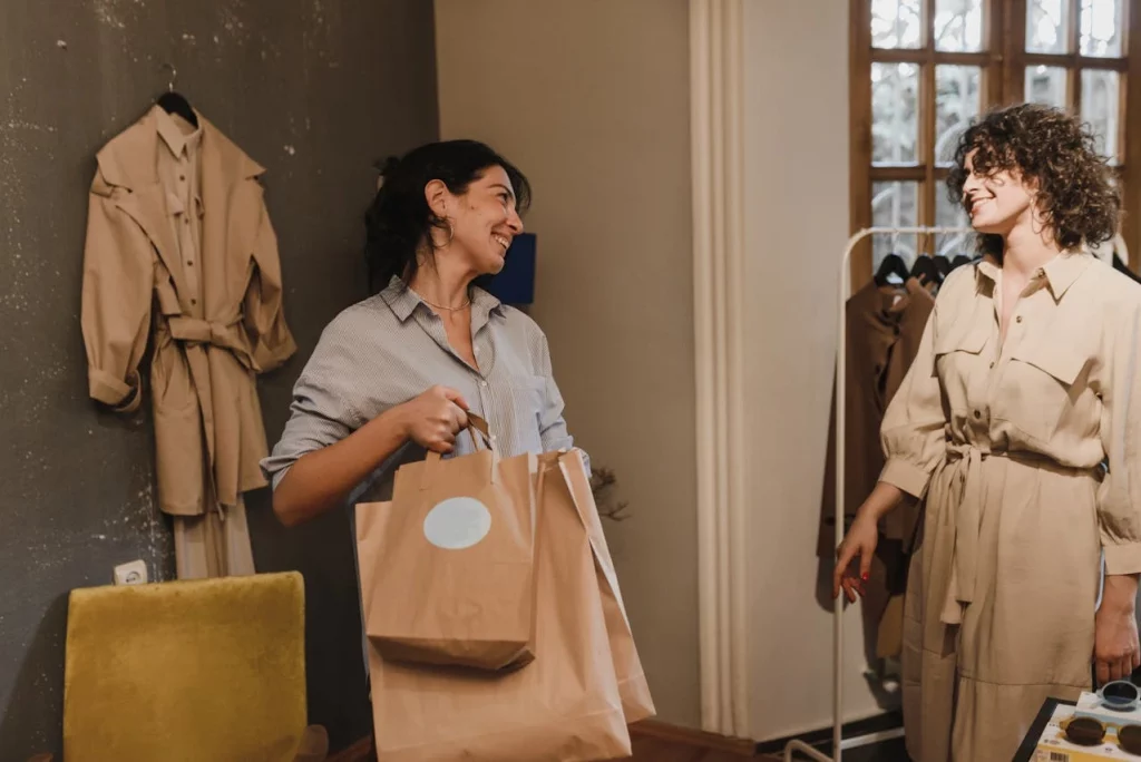 pexels-arina-krasnikova-5424974 Managing retail operations with ease, the image shows a woman in blue shirt holding paper bags while other woman in curly hair smiling
