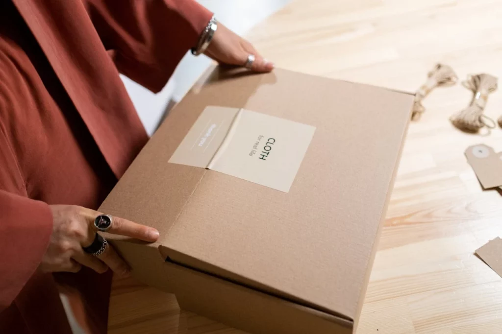 pexels-ron-lach-9853462 A cardboard box with a tag mentioning Cloth on it while being closed by someone with rings on their fingers