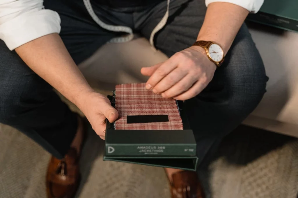 Yushkova Designs A tailor with white wrist watch holding sample of cotton fabric with different designs