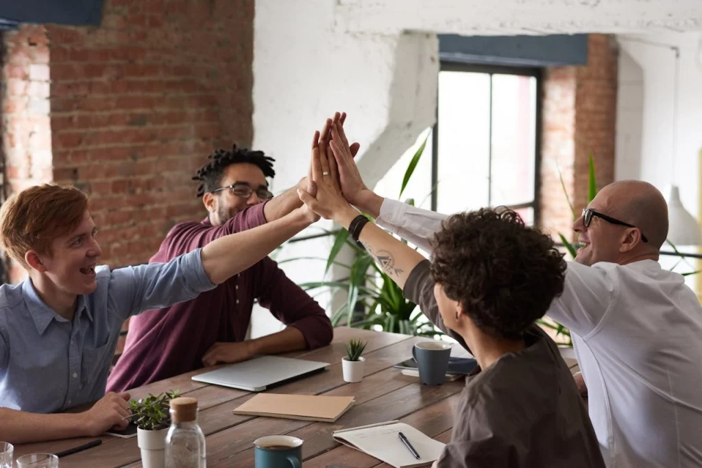 Group of colleagues cheering up at the table and giving each other a high five