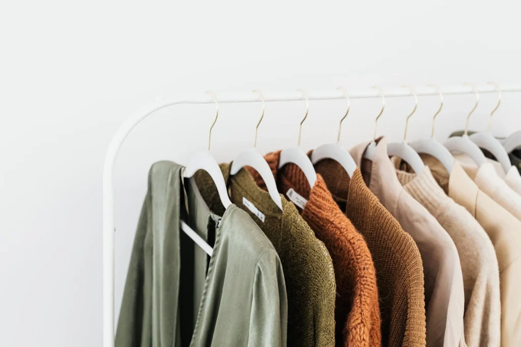 Private Label Strategy of a Minimalist fashion clothing rack with neatly hung neutral-tone garments on white hangers against a clean white background, showcasing a private label apparel aesthetic. Modern boutique style wardrobe display featuring earthy colors and simple fashion organization.