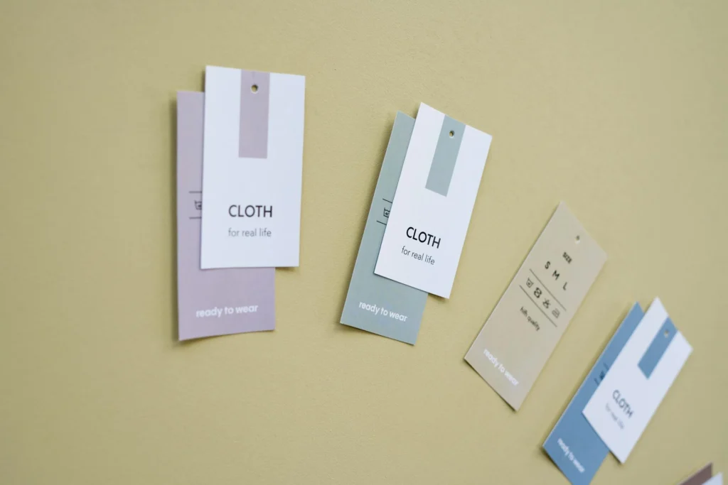 Assorted minimalist clothing brand tags and apparel labels arranged on a pastel surface, symbolizing private label branding and fashion identity design. Clean typography and soft color palette representing modern garment packaging concepts.