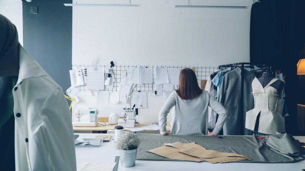Designer reviewing garments and patterns in a fashion studio, representing apparel product development and supply chain planning. The image reflects fashion prototyping, garment construction, and private label production processes.