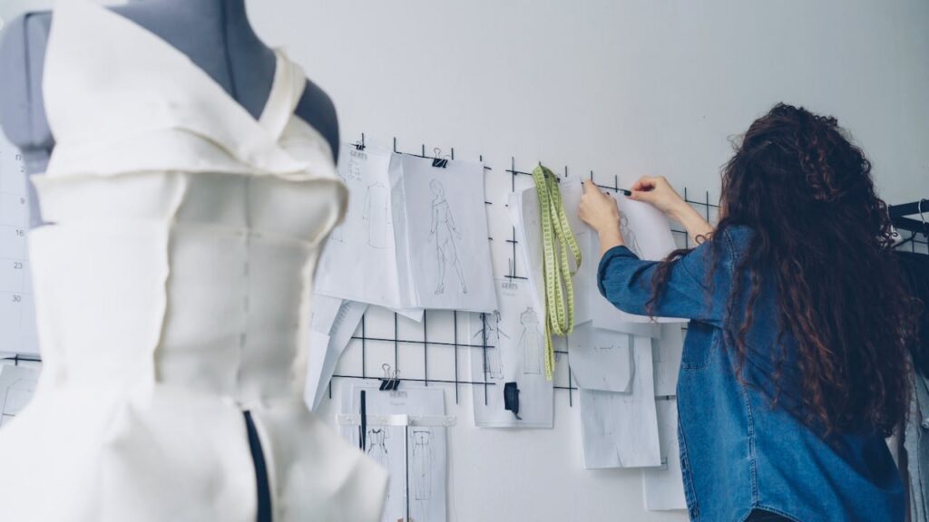 Fashion designer organizing sketches and measuring tools in a studio, highlighting apparel sampling, technical design, and product development workflows. This image represents fashion sourcing strategy and end-to-end supply chain preparation.